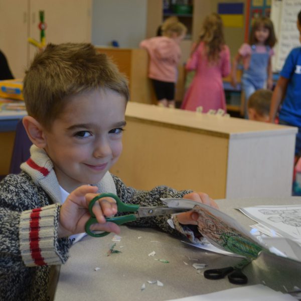 kindergarten student cutting paper with scissors
