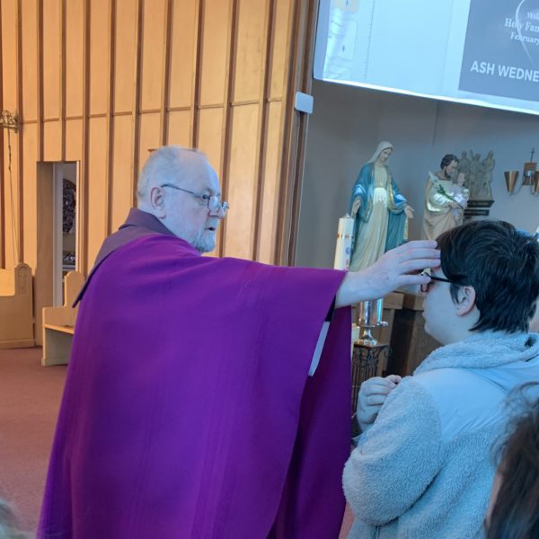 Priest applying ashes to forehead of student at Ash Wednesday mass