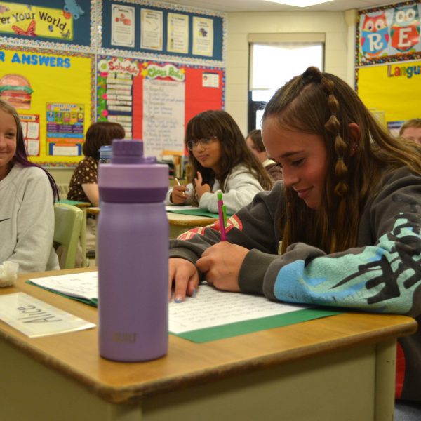 student writes while another student smiles at her