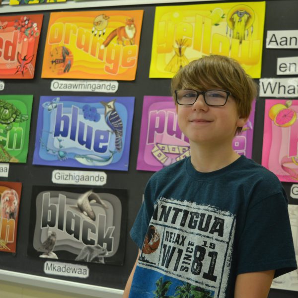Student stands in front of an Ojibway language comparison chart