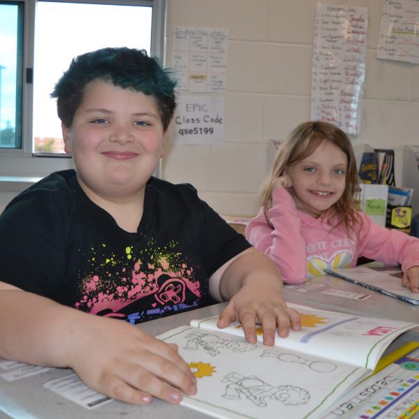 Two students sitting at their desks smiling for the camera