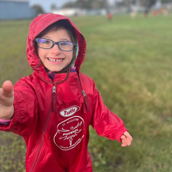 Kindergarten student in raingear reaching for camera