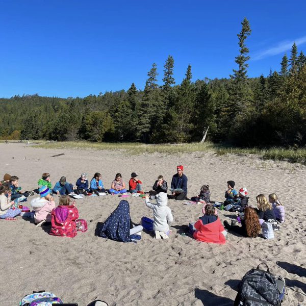 Students sitting in a circle on a beach learning about Indigenous culture