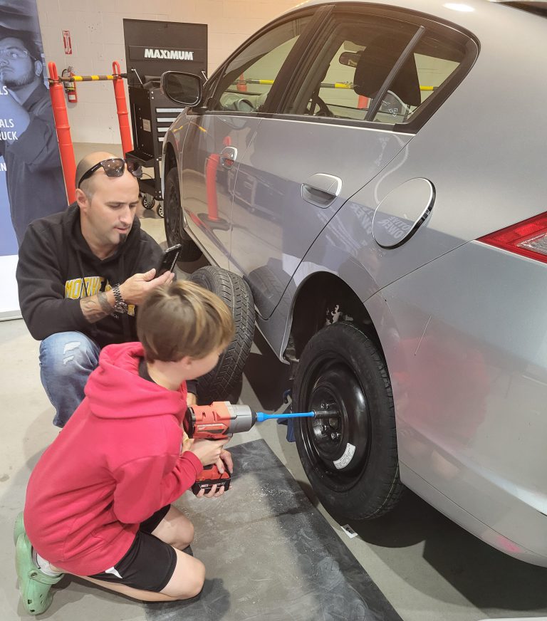 A student uses a tool to tighen a lug nut on an automobile