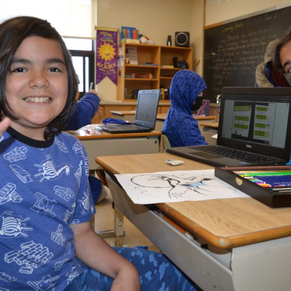 Student shows the peace sign while sitting at his desk