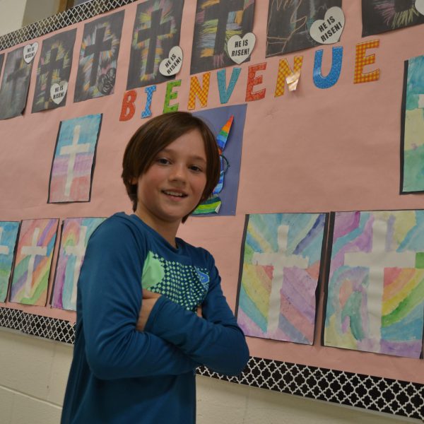 Student stands in front of bulletin board with French wording