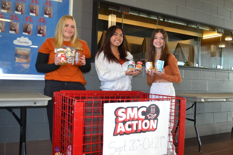 Three St. Mary's College students show food items collection in the SMC Action food drive