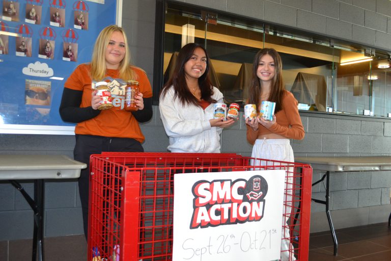 Three St. Mary's College students show food items collection in the SMC Action food drive