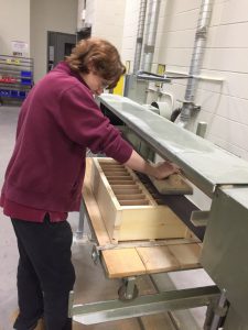 A student uses belt sander on piece of cell phone holder