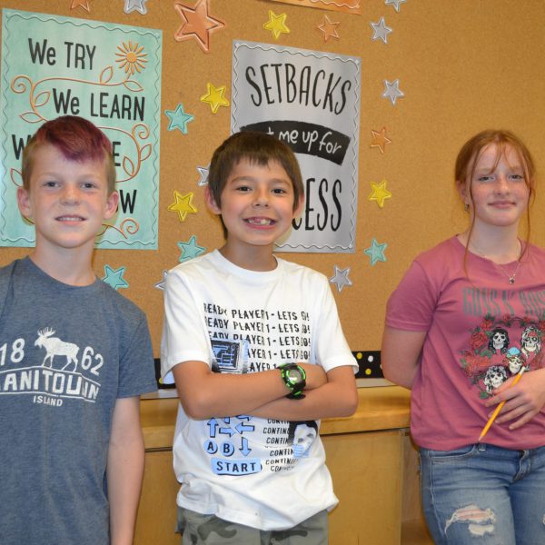 three students standing in front of bulletin board